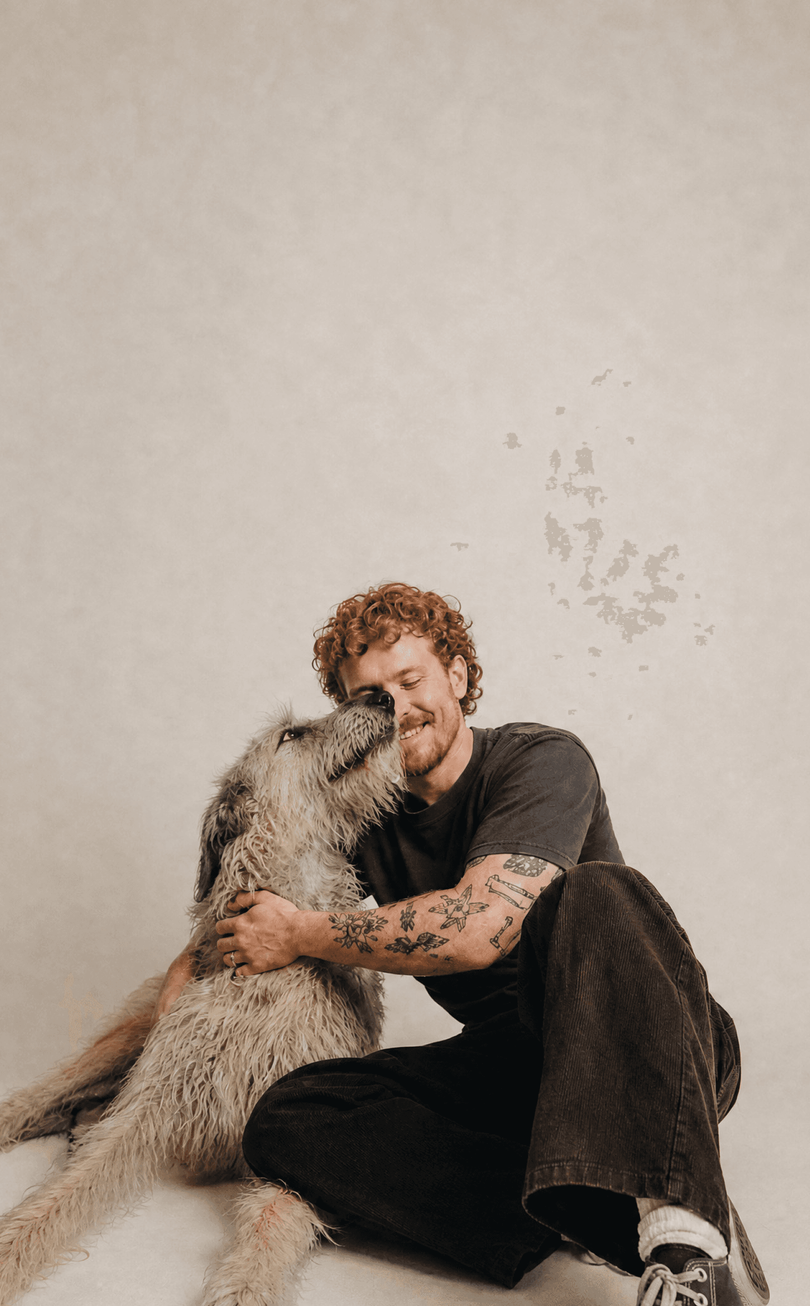 A young man sits on a studio floor hugging his Irish wolfhound, who leans in to nuzzle his face.